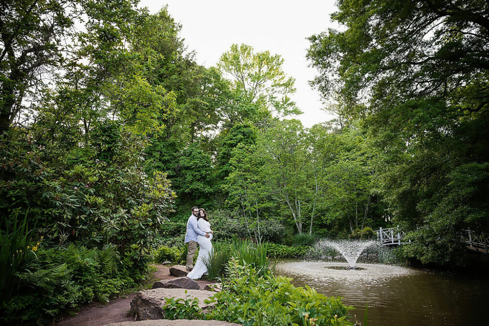 Man holding his pregnant wife lovingly for their couple pregnancy photos taken in a garden for their summer garden maternity session in Pricnceton, New Jersey.