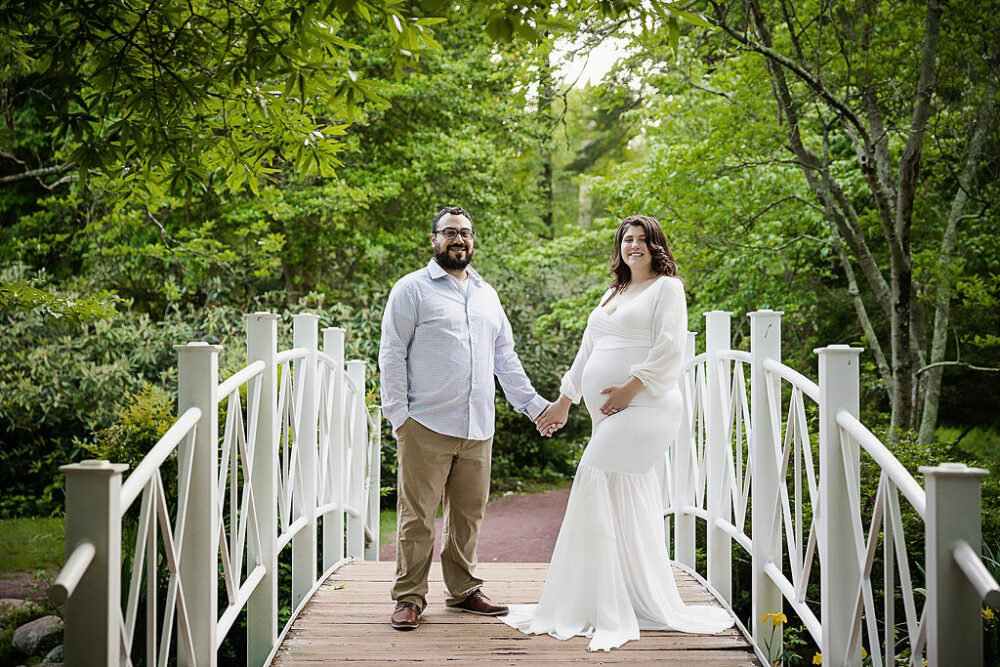 Man and woman holding hands on bridge for their professional couple pregnancy photos for their Spring Garden maternity session in Mount Holly, New Jersey.