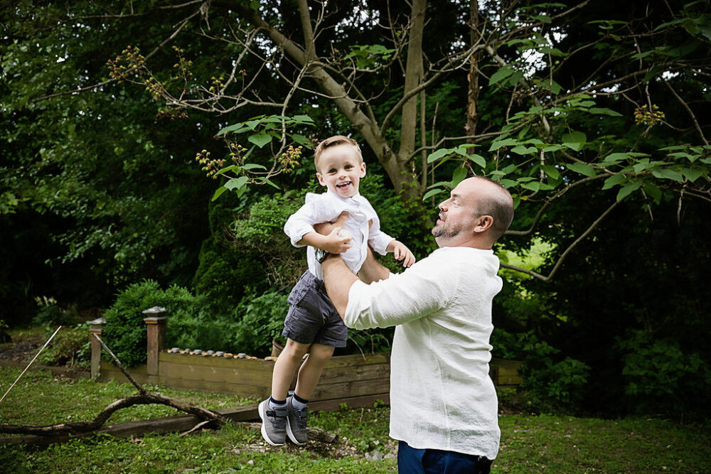 Candid portrait of father tossing son in air in backyard for their family photos taken in Mount Holly, New Jersey.
