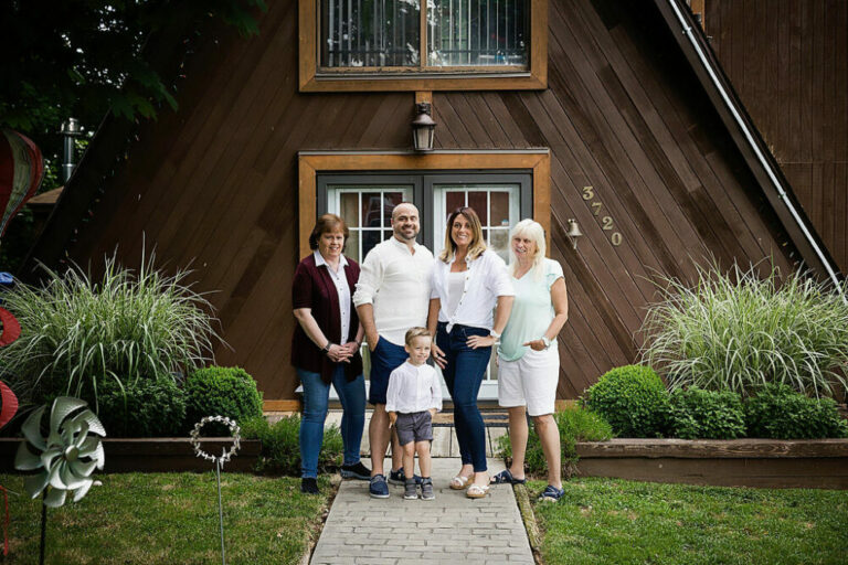 Mother and father, with their toddler son, and his grandmothers standing in front of their family home for updated family portraits taken in Burlington, New Jersey.