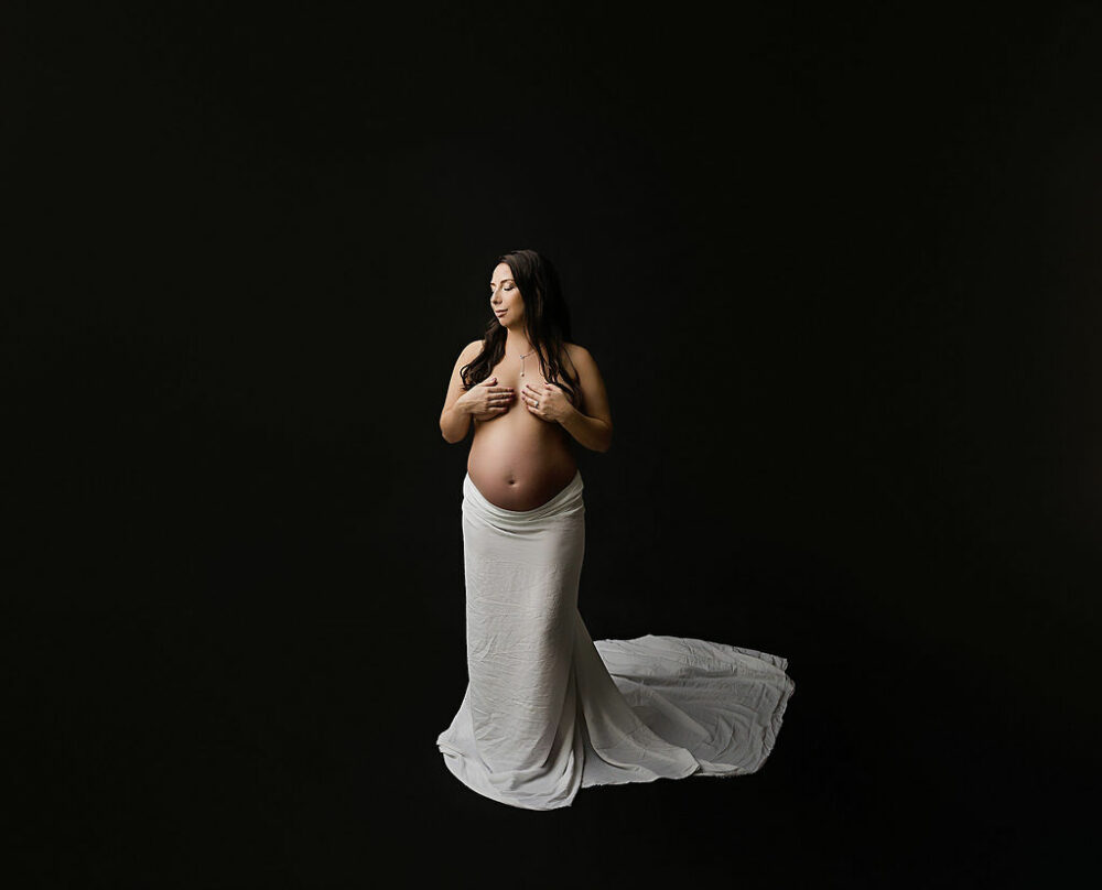 Pregnant woman posing against black background wearing skirt for her nude in-studio maternity session in Southampton, New Jersey.