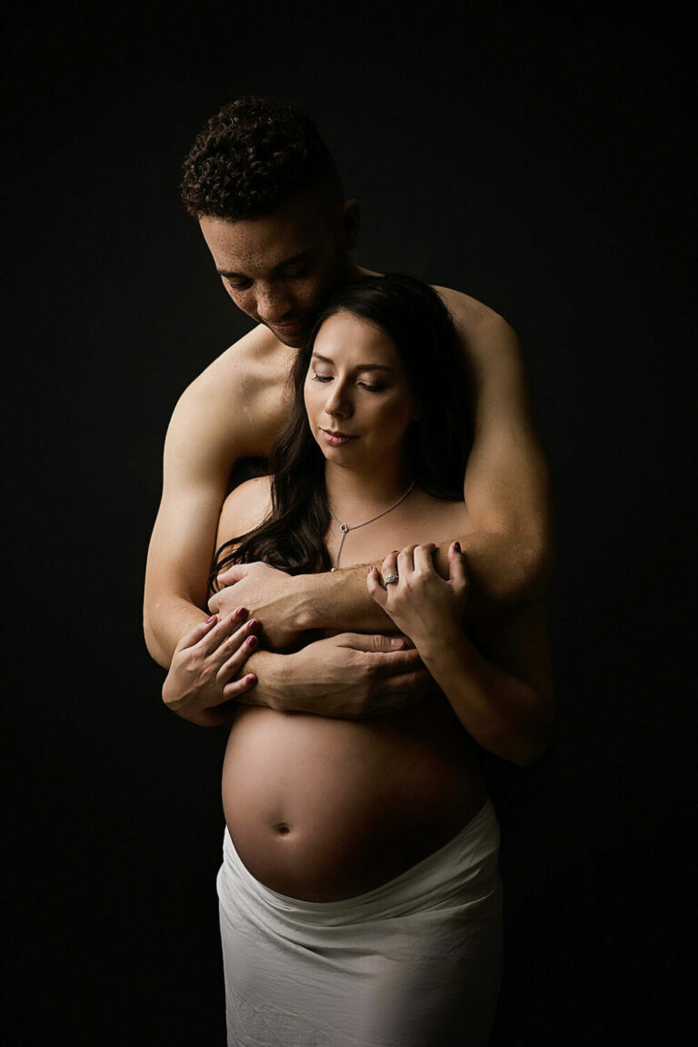 Close up maternity portrait of husband, holding pregnant wife for their nude in studio maternity session taken in Hamilton, New Jersey.