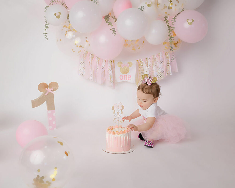 Toddler girl, touching Minnie mouse, smash cake for her pink first birthday session taken in Camden, New Jersey.