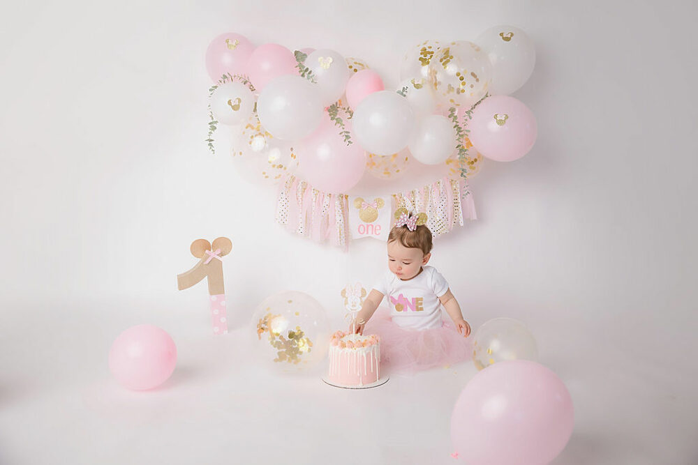 Toddler girl, wearing skirt and bow on head with cake for her pink first birthday session in Glassboro, New Jersey.