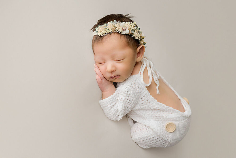 Newborn portrait of Sleepy, baby girl, wearing flowery headband and knit outfit for her in studio newborn session In Woodbury, NJ.