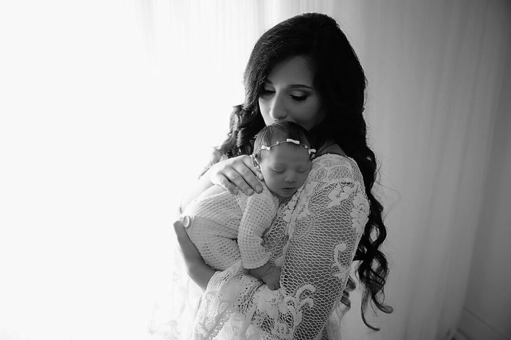 Black and white portrait of mother, holding her sleeping newborn girl in arms for her in studio, newborn photography taken in freehold, New Jersey.