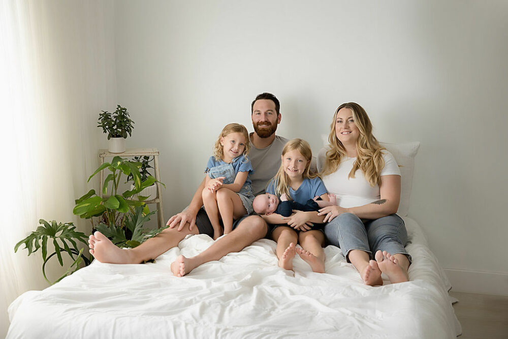 Family of five sitting on photography bed prop for their newborn family photos taken in studio in Morristown, New Jersey.