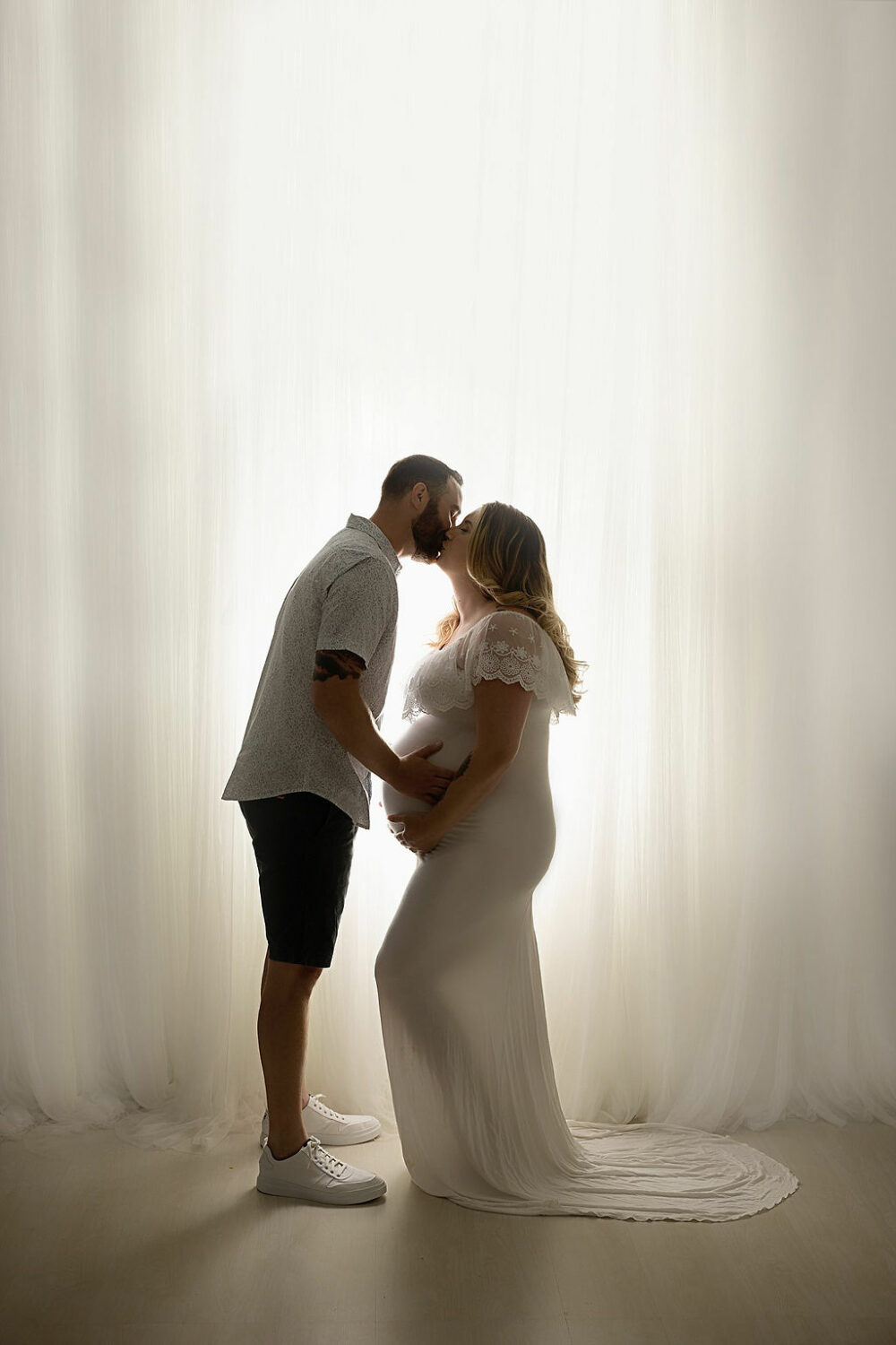 Husband and wife kissing and holding wife’s belly for her cute maternity pictures taken in studio for her blue maternity session taken in Southampton, New Jersey.
