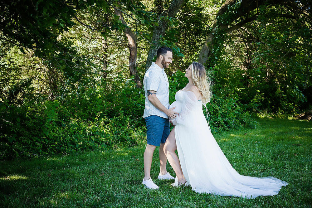 Husband and wife looking at each other lovingly while they are both holding her pregnant belly for a couple maternity ideas taken outside in Essex county, New Jersey.