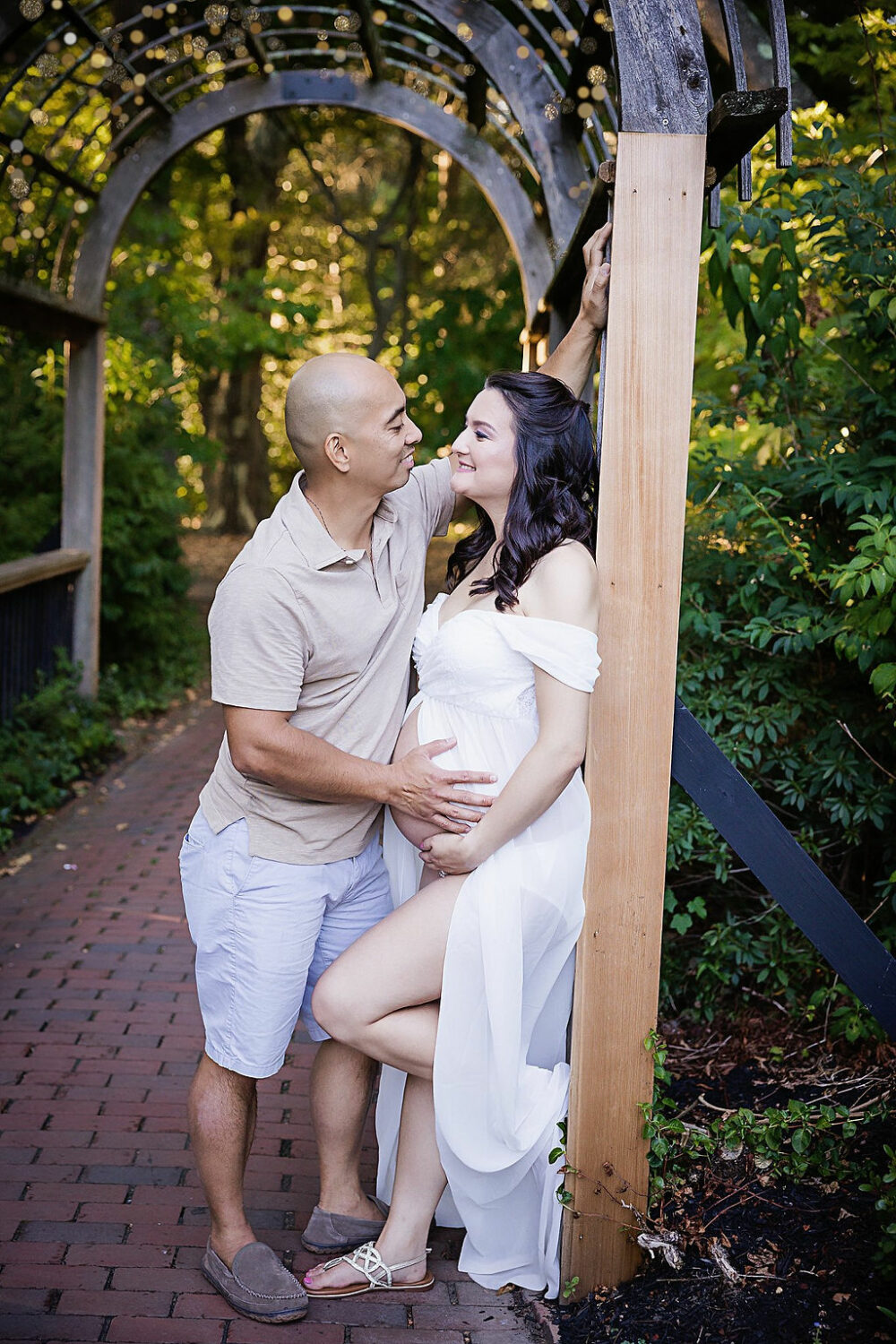Intimate photo of couple staring into each other's eyes while leaning on post and holding her belly for their maternity portraits taken in Burlington, New Jersey.