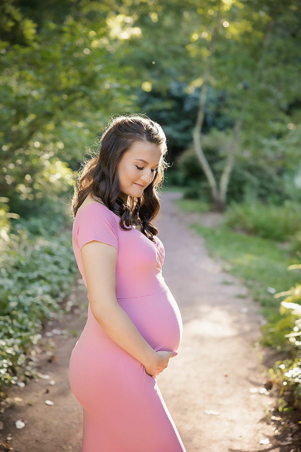 side profile of pregnant woman in maternity dress holding belly for her outdoor maternity pictures taken in Cherry Hill, New Jersey.