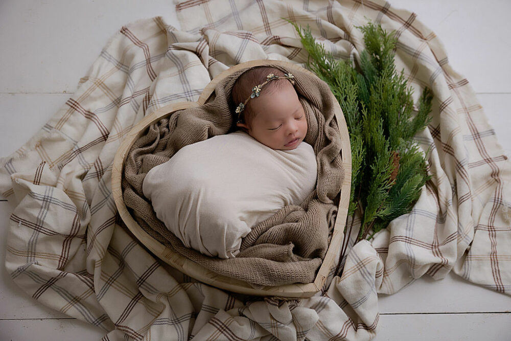Newborn girl wrapped in swaddle and dainty headband and sleeping in heart shaped newborn photography prop for her milestone newborn session taken in Freehold, New Jersey.