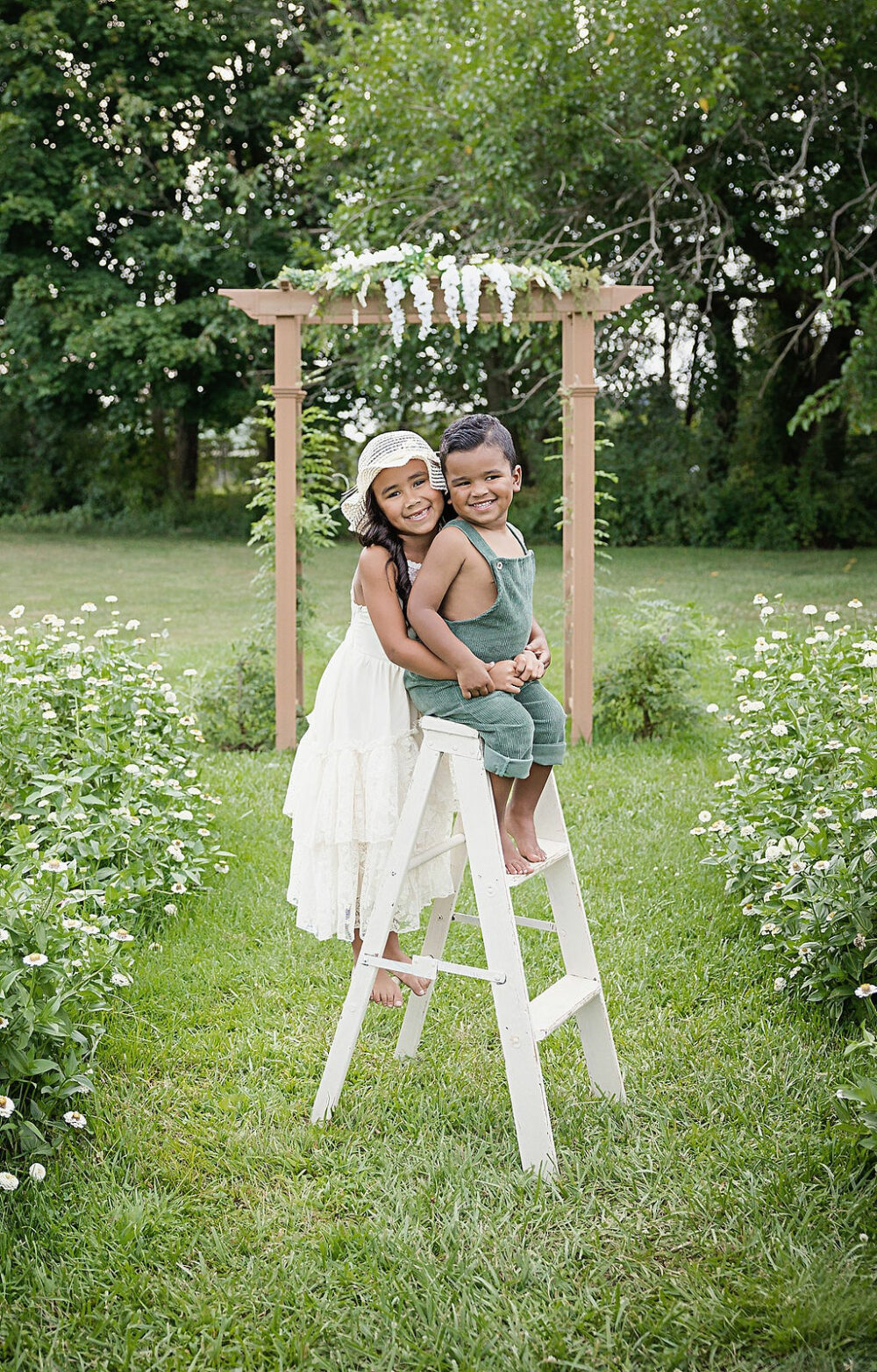 Big sister hugging younger brother while on a ladder for flower mini sessions and flower garden taken in Mount Laurel, NJ.