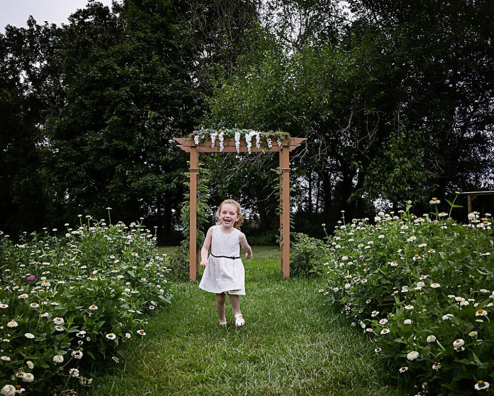 Young girl running towards camera smiling in Flowerfield for her flower mini sessions taken in Moorestown, New Jersey.