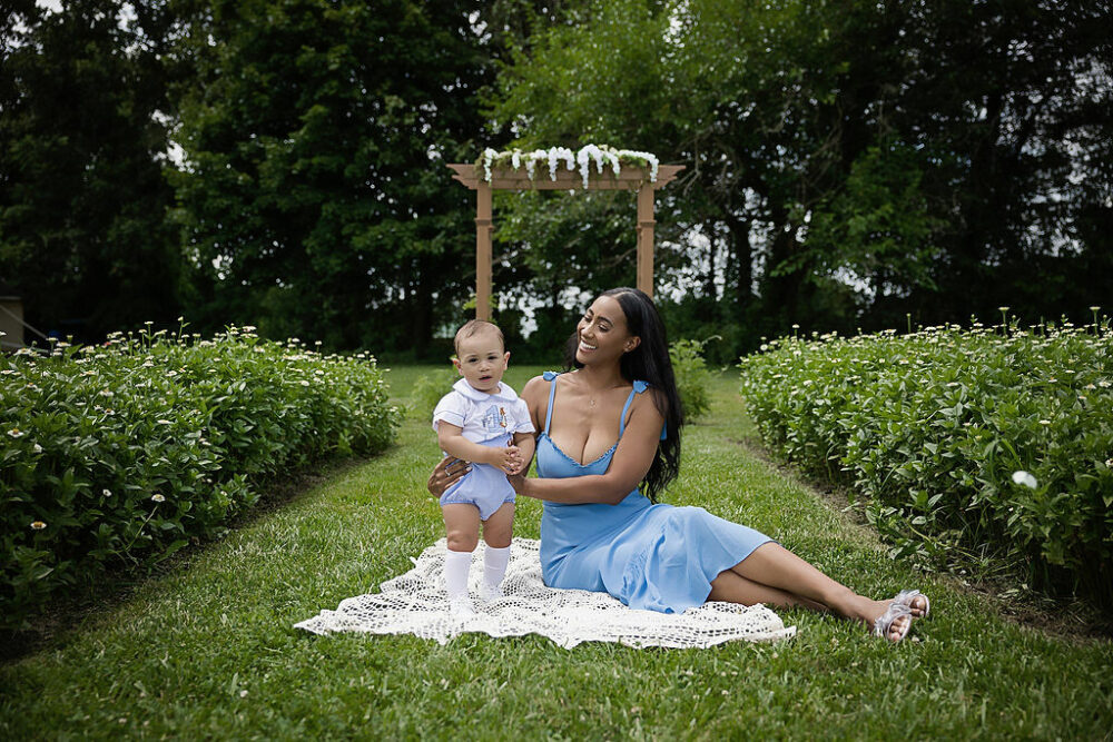 One-year-old boy with his mother and garden, sitting on blanket for his baby milestones photography taken during his peter rabbit, first birthday session taken in Monmouth county, New Jersey.