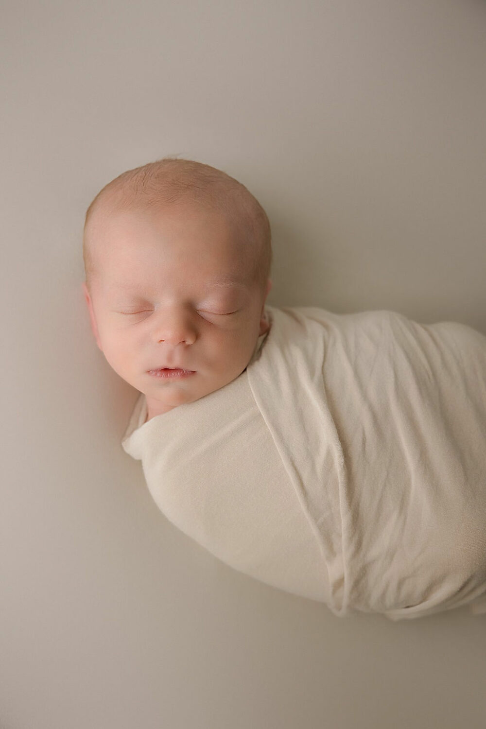 Sleeping newborn boy posed for his infant portrait, sleeping in swaddle for his professional, baby pictures, taken during a twin neutral newborn session in Moorestown, New Jersey.