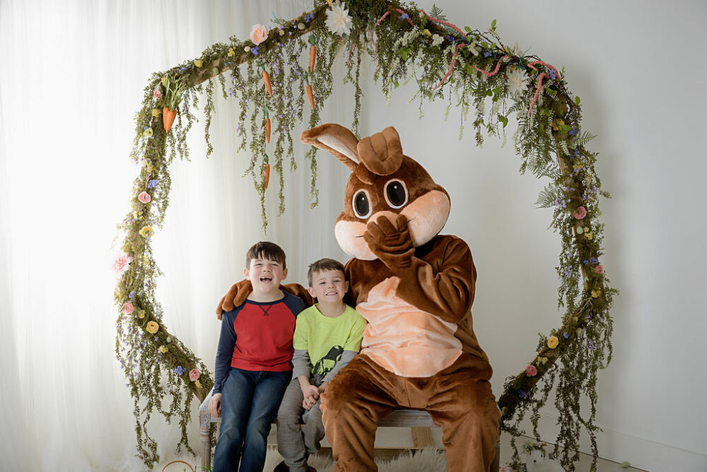 Man in brown Easter bunny costume sitting next to two young boys all looking and smiling a camera for their Easter mini session in South Philadelphia.