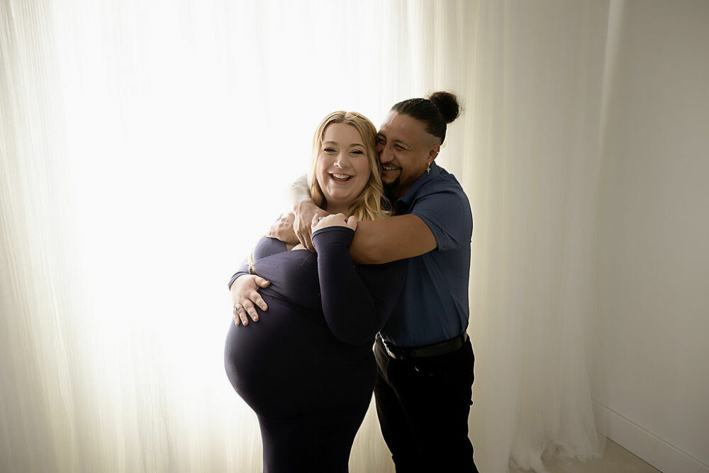 Man and woman laughing and holding each other for an in-studio blue maternity session in Cherry Hill, New Jerse