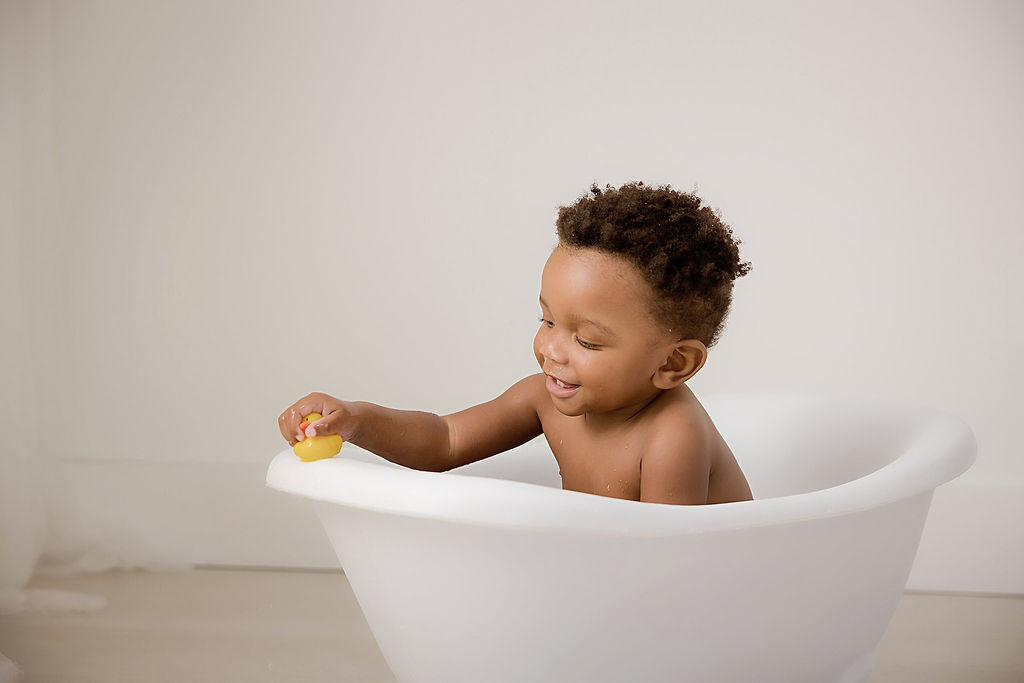 Toddler boy in bathtub photography prop for his portrait photography during his Carnival first birthday session in Camden, New Jersey.