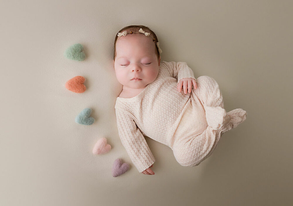 Infant girl, sleeping on back, adorned with felt hearts, wearing cute newborn outfit and headband for her Nicu in studio newborn session in Trenton, New Jersey.