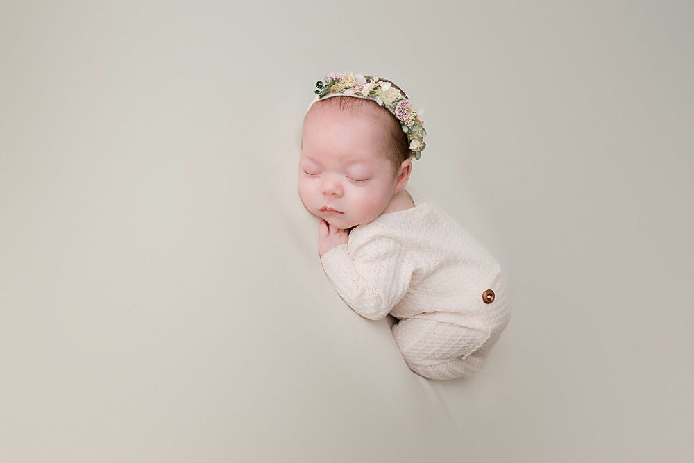 Newborn girl, sleeping in frogs pose wearing newborn outfit and headband sipping on beanbag for her baby picture ideas in Camden, New Jersey.
