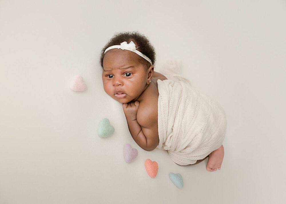 Close-up of newborn girl laying on tummy and swaddle and matching headband with colorful felt hearts for her newborn photography session in Chesterfield, New Jersey.