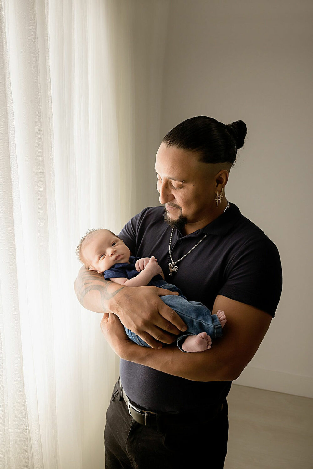 Man holding his newborn son in his arms while looking at him and baby is looking at camera for a blue newborn session taken in Eastampton, New Jersey.