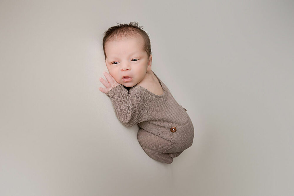 Newborn boy awake and laying on his stomach with legs tucked in for his professional infant photography taken in Wrightstown, New Jersey.