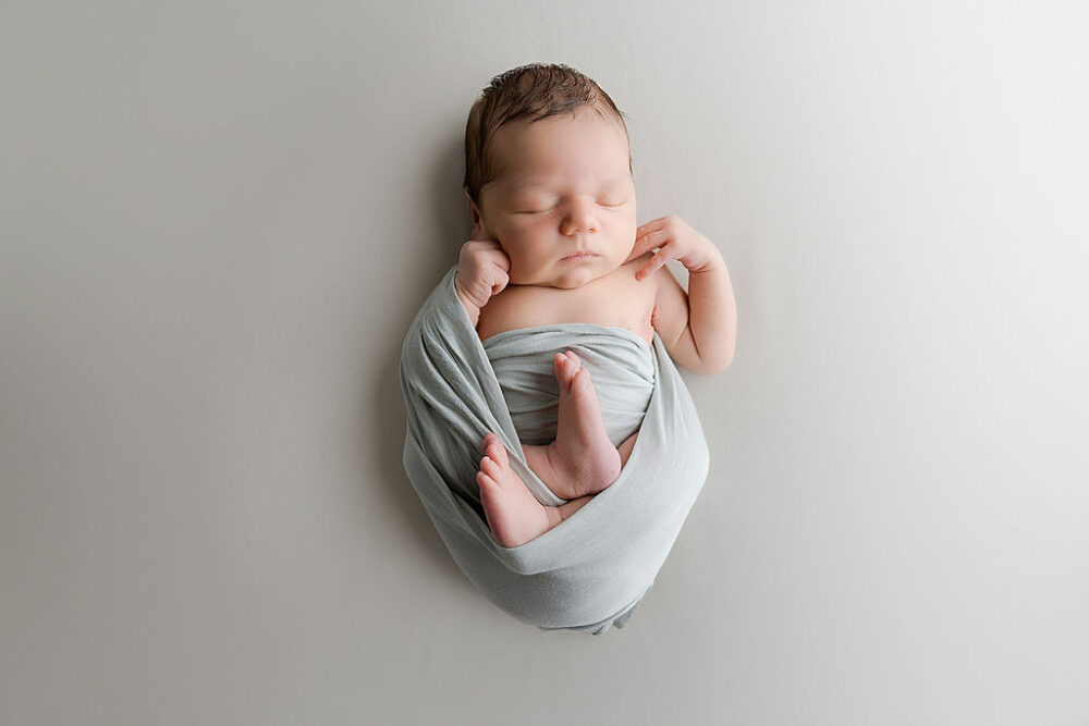 Infant boy in swaddle, sleeping on back, and with hands and feet exposed for his put him right in Home Newborn session, taken in Morristown, New Jersey.