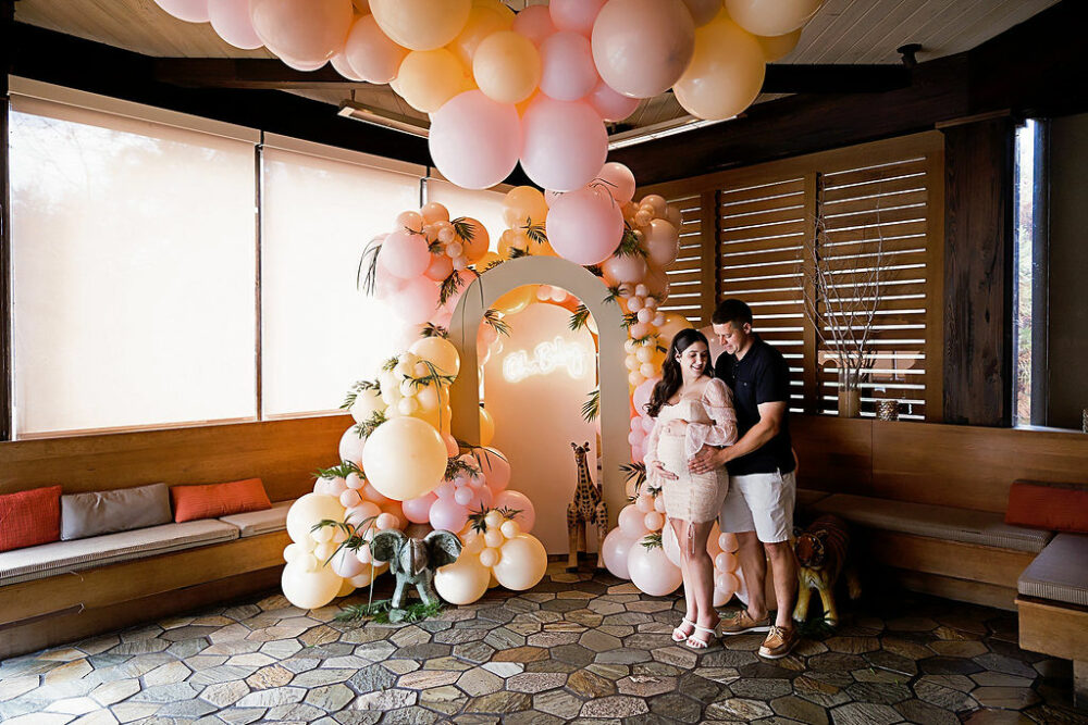 Man and woman standing next to baby shower, decorations, holding her belly and restaurant venue for her baby shower photo shoot in Southampton, New Jersey.