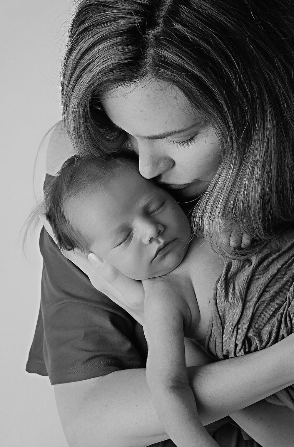 Woman kissing her newborn son while holding him and in her arms for a close-up portrait taken during their green in-studio newborn session in Moorestown, New Jersey.