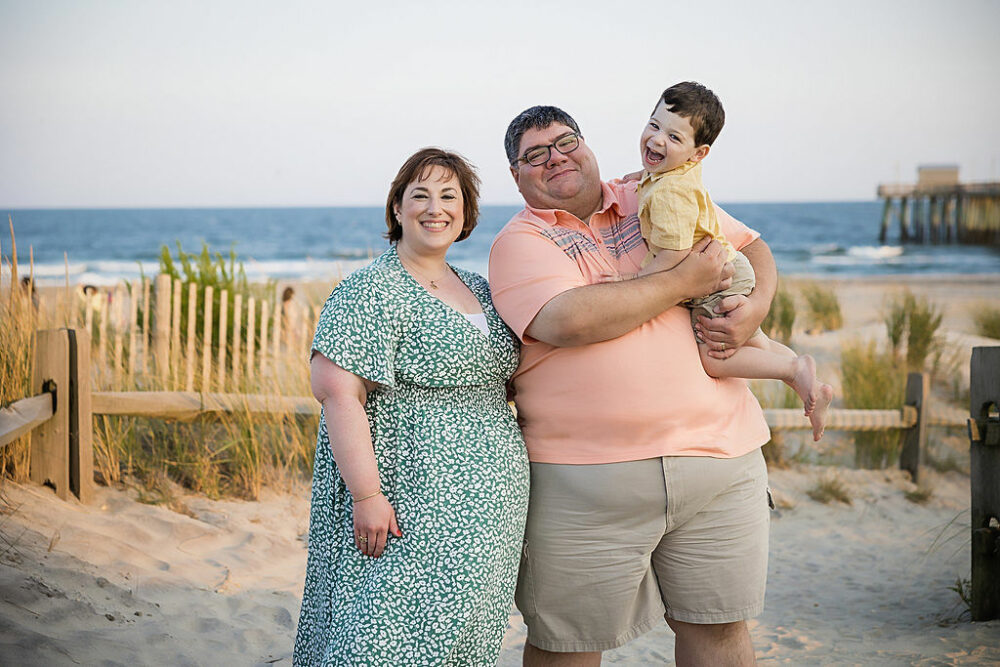 Family Photo ideas the man and woman standing next to each other while man's holding his son posing for beach pictures in Cape May, NJ.