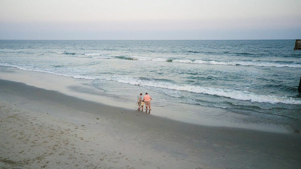 Drone footage of a man and woman walking toward the ocean holding their toddlers hand for their beach photography session in Tom's River, New Jersey.