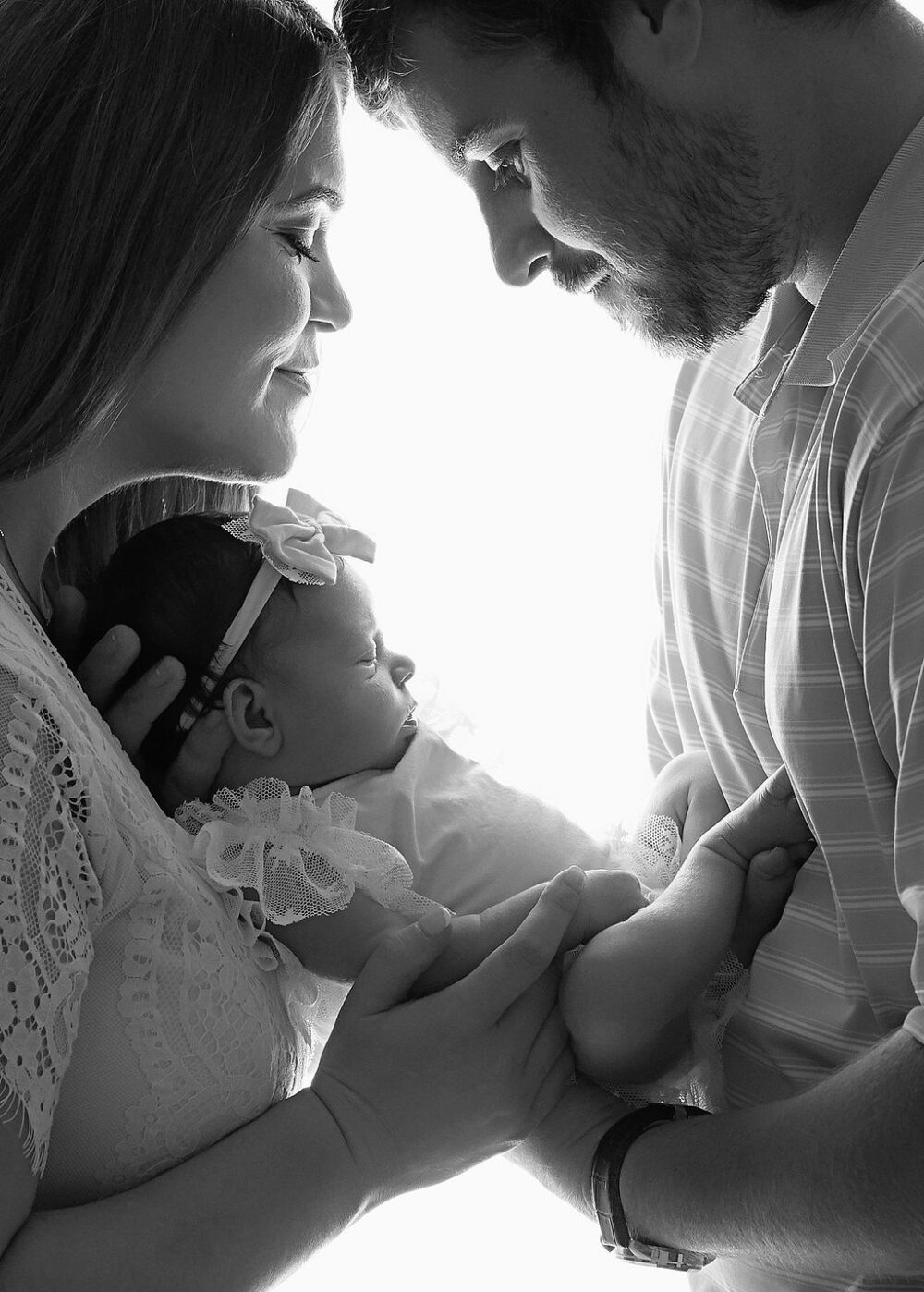 Close-up of a man and a woman holding their daughter in between them as a touch foreheads for their newborn photography session, taken in Camden, New Jersey.