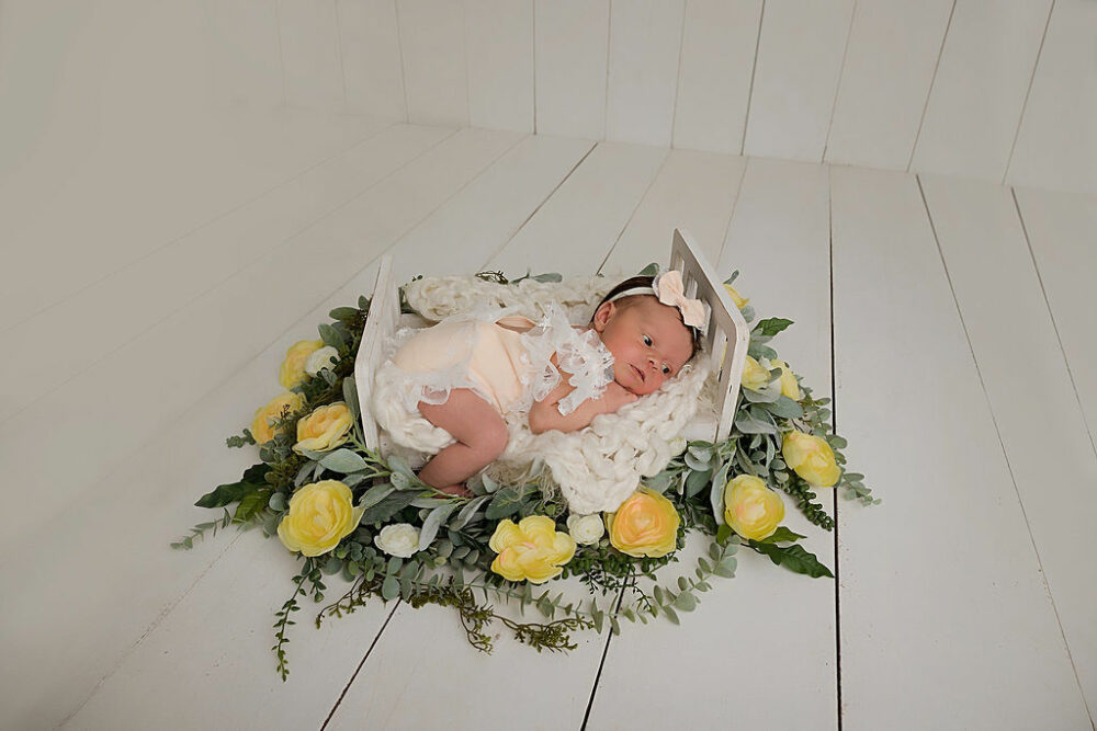 Newborn girl, laying on tummy on crib, photography, propped adorn with greenery and flowers for her neutral in studio newborn session, taken in Burlington, New Jersey.