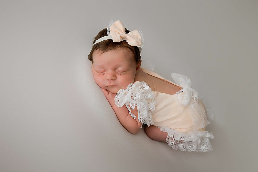 Infant girl sleeping on her tummy with hands and feet tucked in wearing a cute outfit for her neutral in studio newborn session in Monmouth county, New Jersey.
