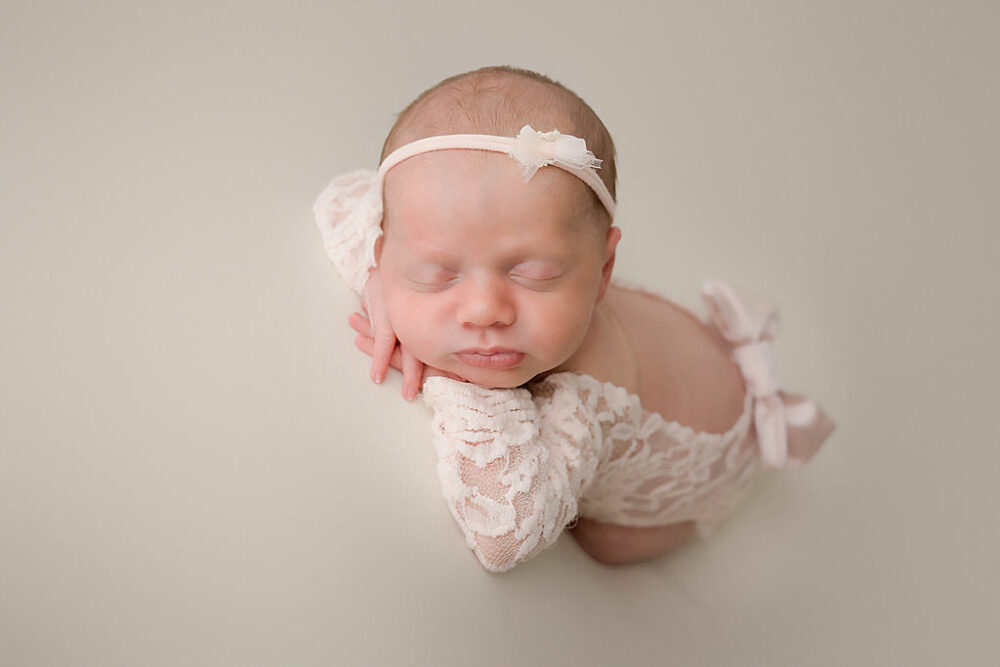 Close-up of infant girl sleeping with her head, rested on her hands taken for her newborn pictures for her pink in studio newborn session in Burlington, New Jersey.