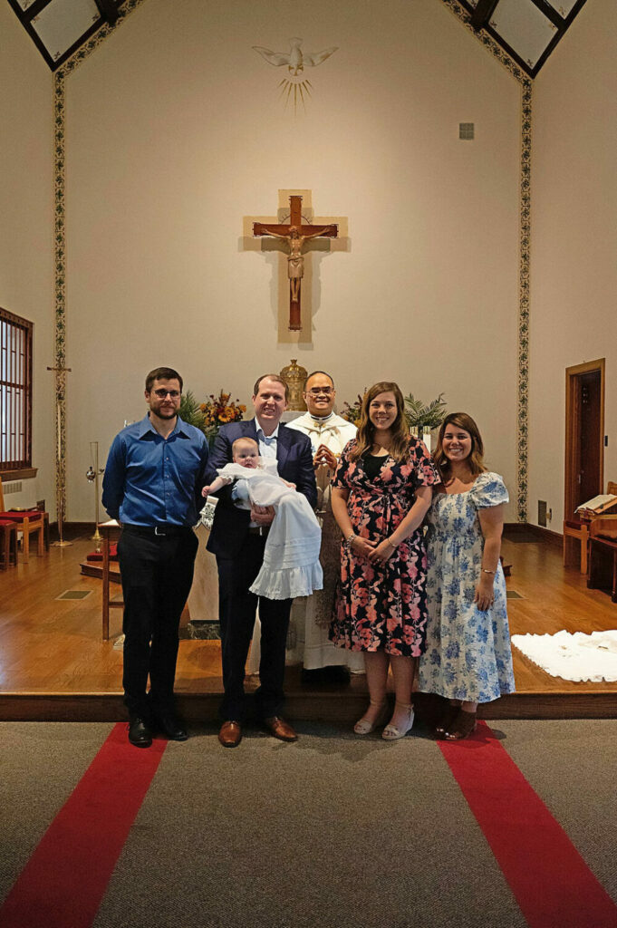 Family session of new parents and their appointed godparents standing in front of church altar with Pastor behind them for their daughters baby baptism and family session taken in South Jersey.