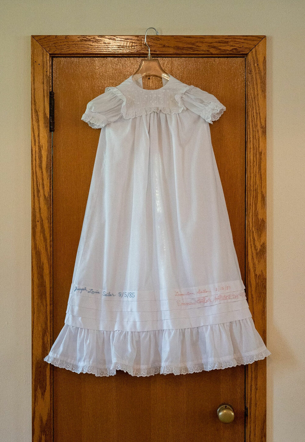 Baptism dress hanging and displayed on door inside church for a baby baptism and family session in Mount Laurel, NJ.