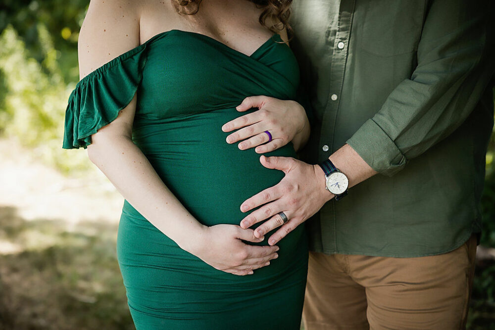 Men and women standing next to each other, facing forward, and both holding women’s belly posing for their fall in studio maternity session in South Jersey.