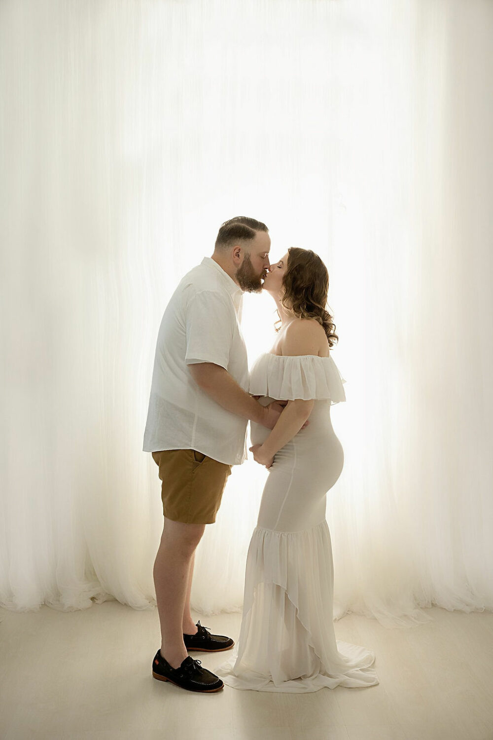 Men and women facing each other and kissing, while holding woman’s belly for their maternity photos, taken in studio in Eastampton, New Jersey.