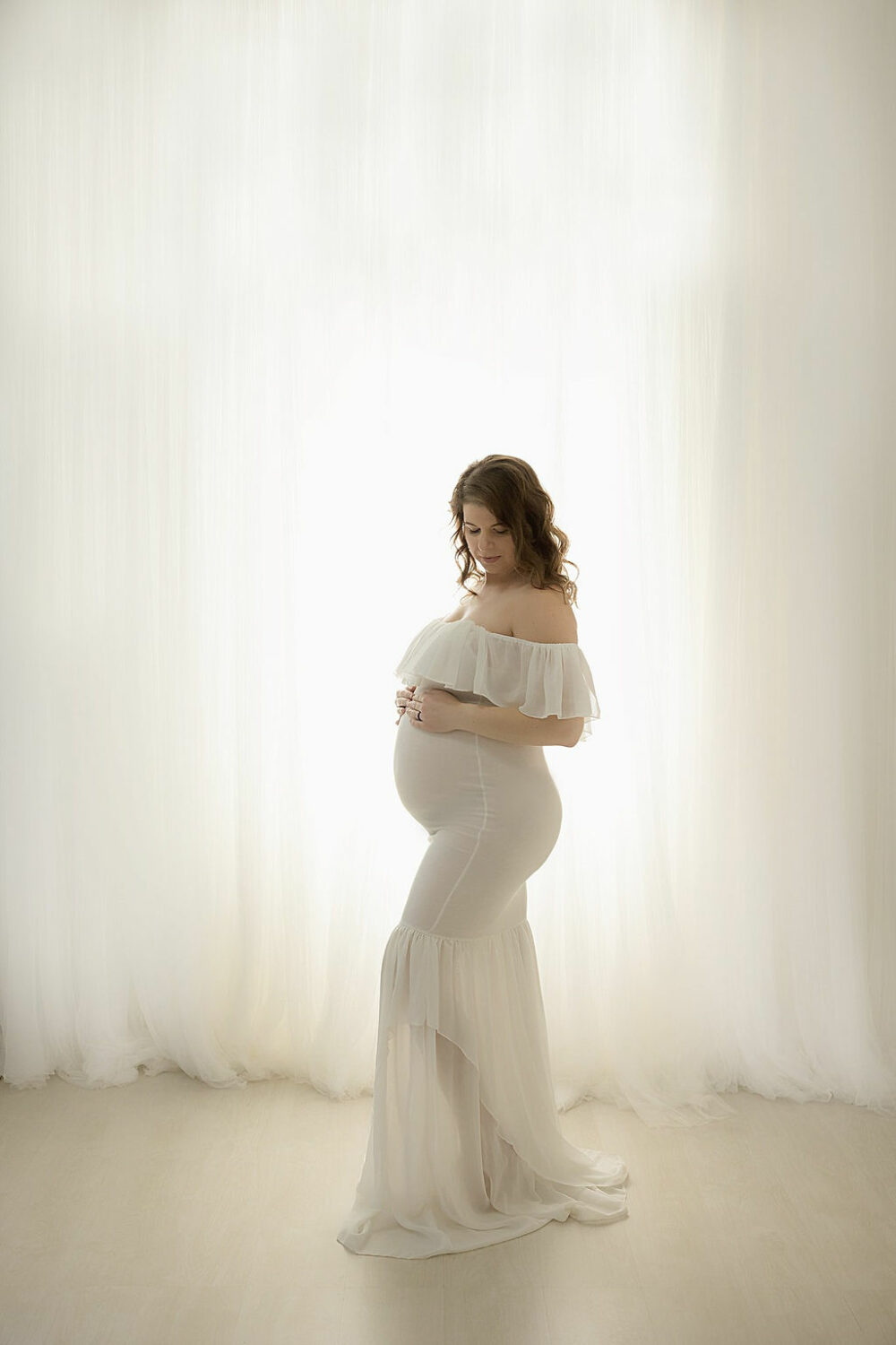 Woman wearing dress standing in front of light in bright background posing for her and Maternity Photoshoot, taken in Southampton, New Jersey.