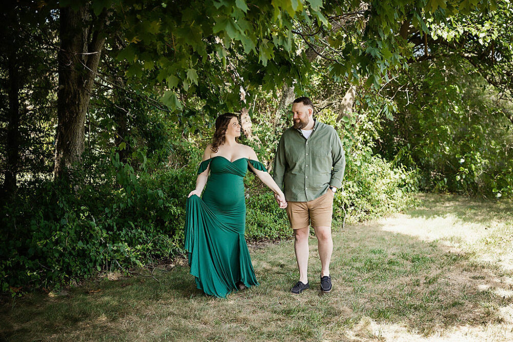 Man and woman facing forward, but looking at each other, while holding hands taken during their outdoor maternity session in Crosswicks, New Jersey.