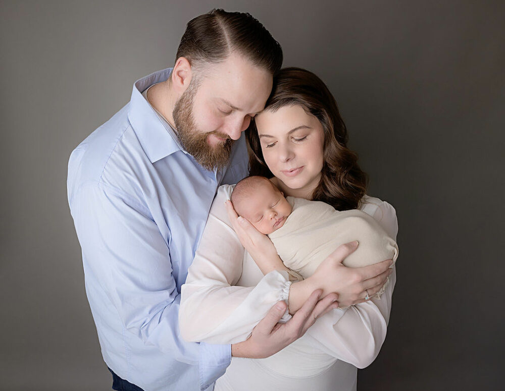 Man and woman holding each other as she holds their newborn son in her arms for their in studio newborn session in freehold, New Jersey.