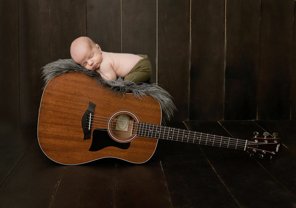 Newborn boy, laying on acoustic guitar, taking during his in studio, newborn session in Pemberton, New Jersey.