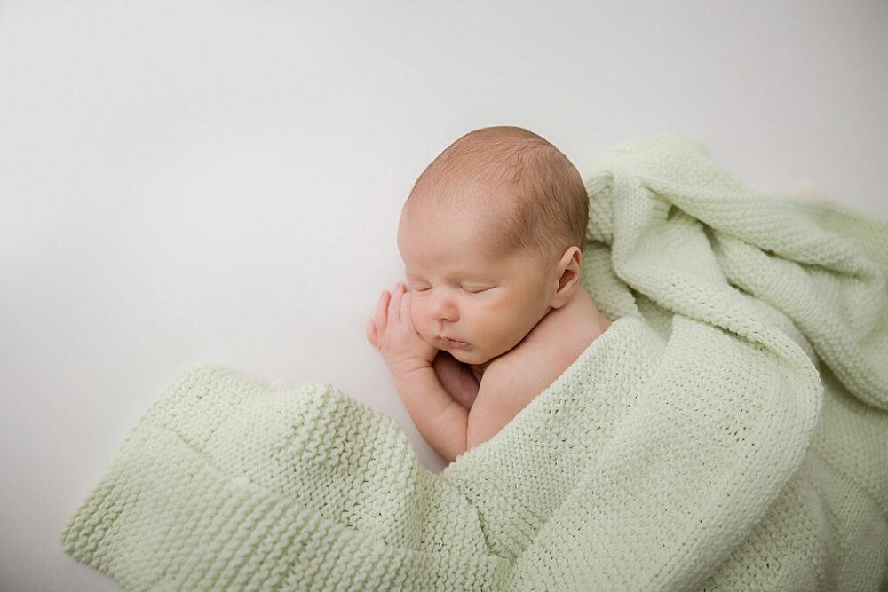 Infant boy, wrapped in blanket, resting on beanbag photography prop for his newborn baby photography session taken in Hamilton, New Jersey.