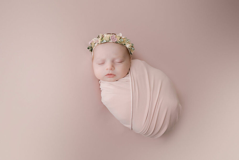 Infant sleeping on back and in swaddle wearing headband for her professional baby pics taken for her in studio newborn session in Camden, New Jersey.