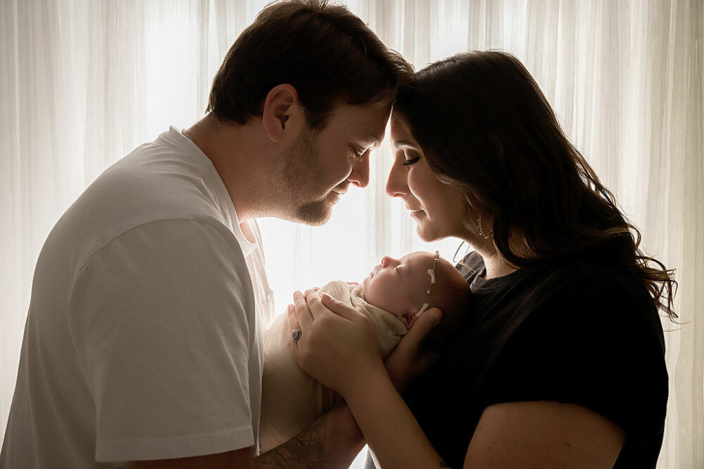 Close up of men and women touching foreheads for holding their infant in between them in their arms for a in studio newborn session for their family pictures in Southampton, New Jersey.