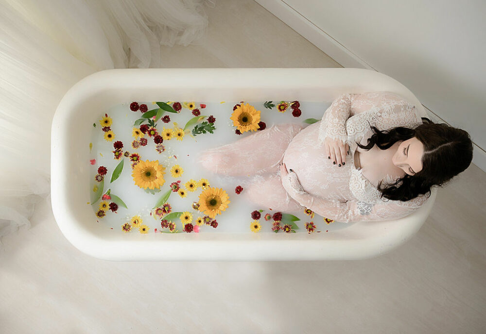 Aerial view of women sitting and posing in milk bath decorated with flowers for her maternity portraits in Eastampton, New Jersey.