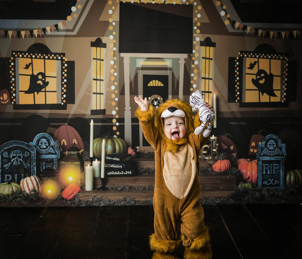 Toddler boy looking at camera with hands raised wearing Halloween costume for an in studio portrait photography in Pemberton, New Jersey.
